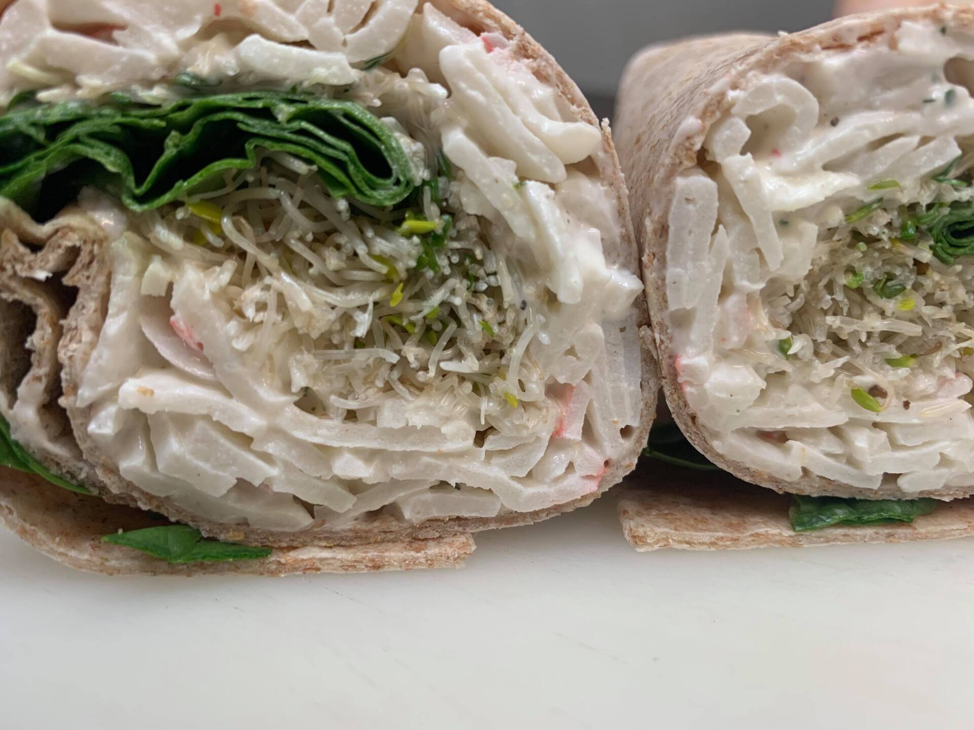 Two halves of a crab salad wrap showing shredded crab, leafy greens, and creamy dressing inside a wheat tortilla.