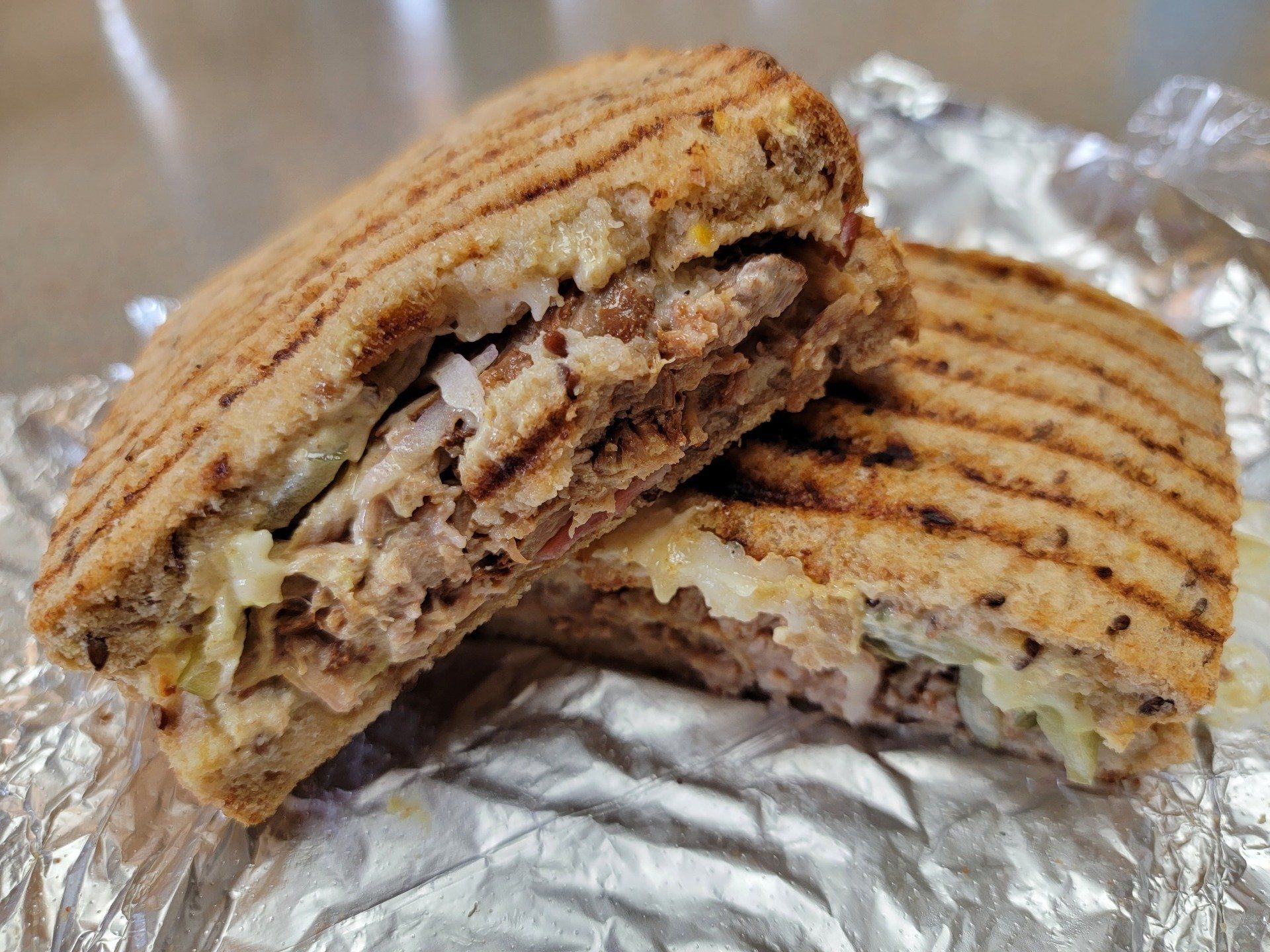 A halved panini sandwich with grill marks on toasted bread, resting on crumpled silver foil.