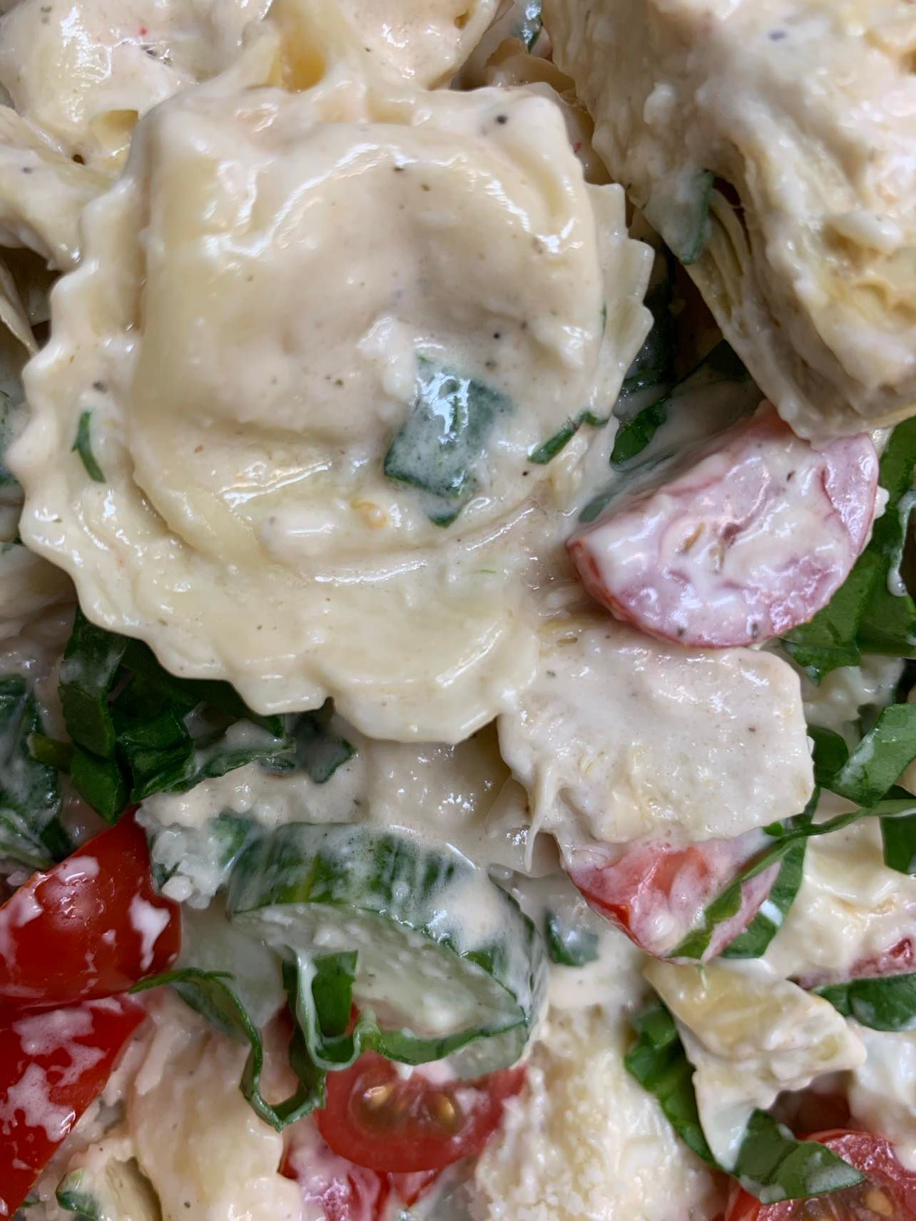 A close-up of a creamy pasta salad with tortellini, sliced cucumbers, cherry tomatoes, and fresh herbs.