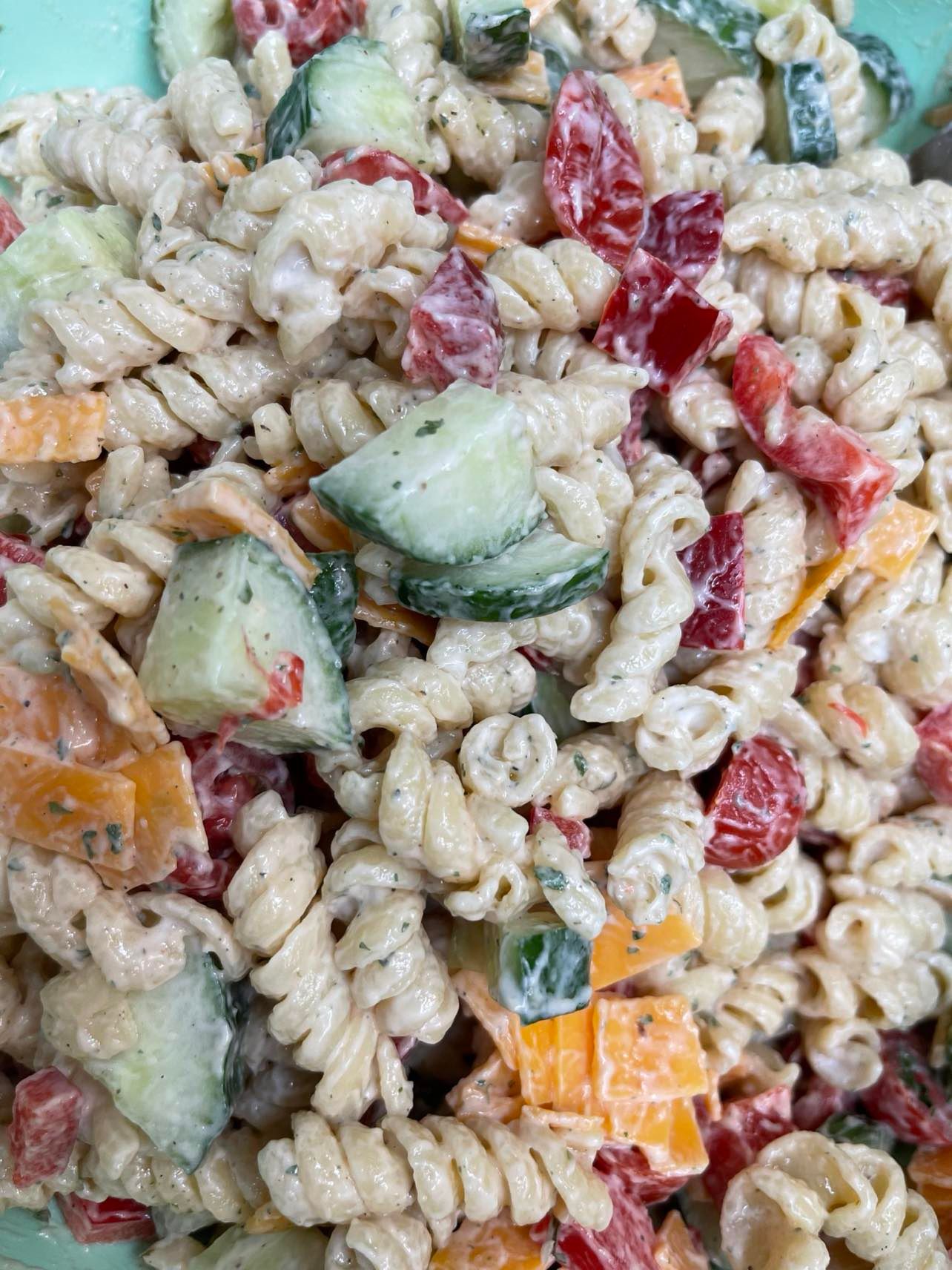 Creamy pasta salad with rotini noodles, chopped cucumbers, red bell peppers, and orange cheddar cheese bits.