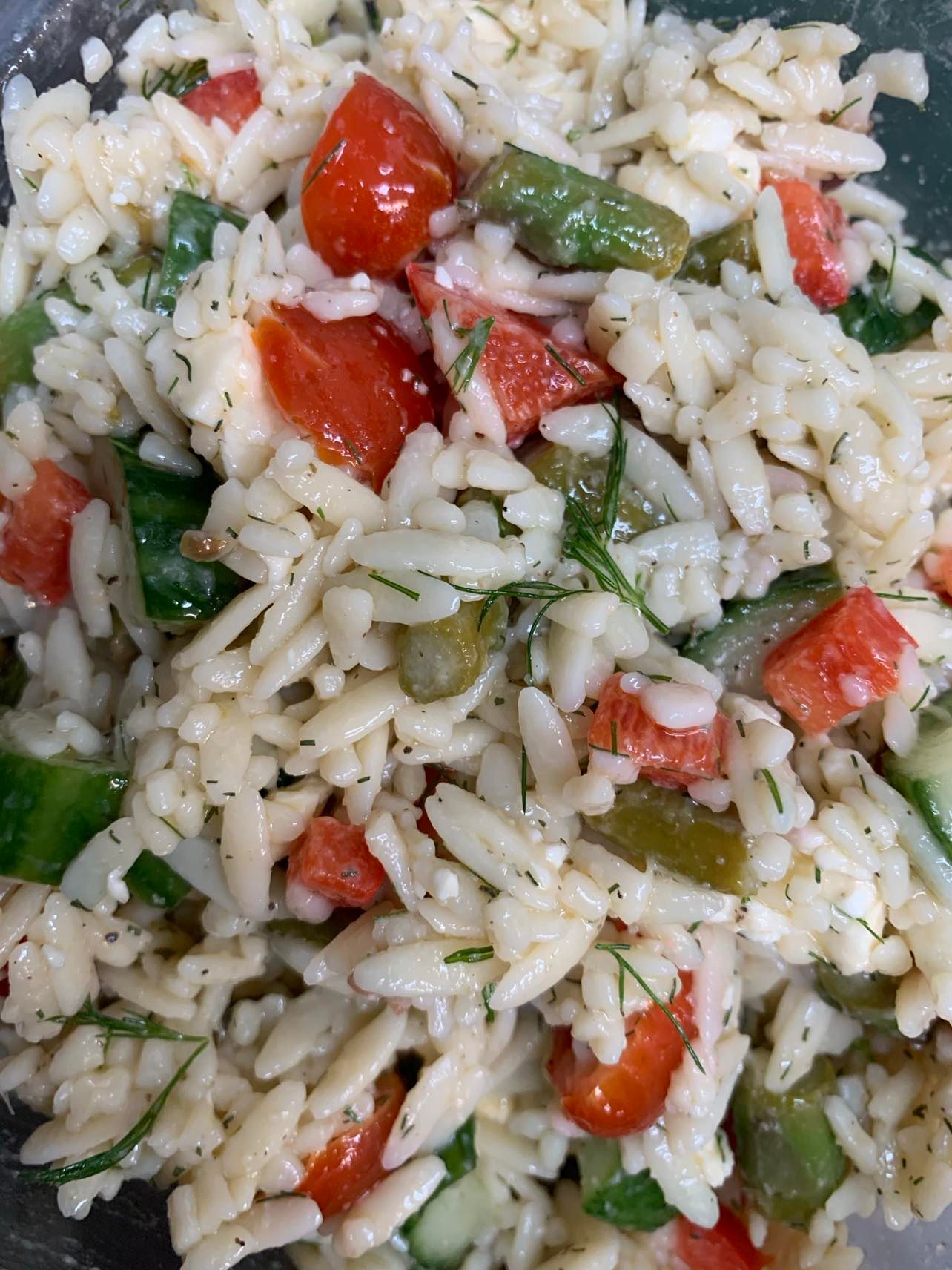 A close-up view of a Mediterranean-style rice salad with chopped red tomatoes, green vegetables, and fresh herbs.