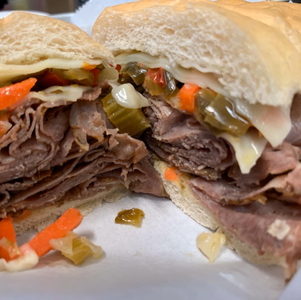 A close-up of a beef sandwich on a crusty roll, topped with melted white cheese and giardiniera relish.