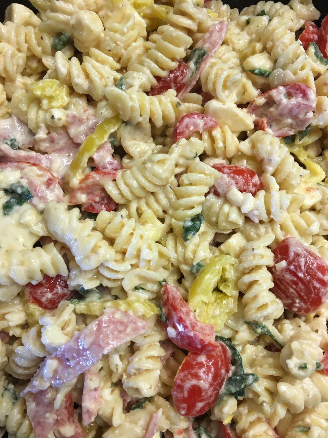 A creamy pasta salad with rotini noodles, cherry tomatoes, sliced meat, and yellow pepper strips.