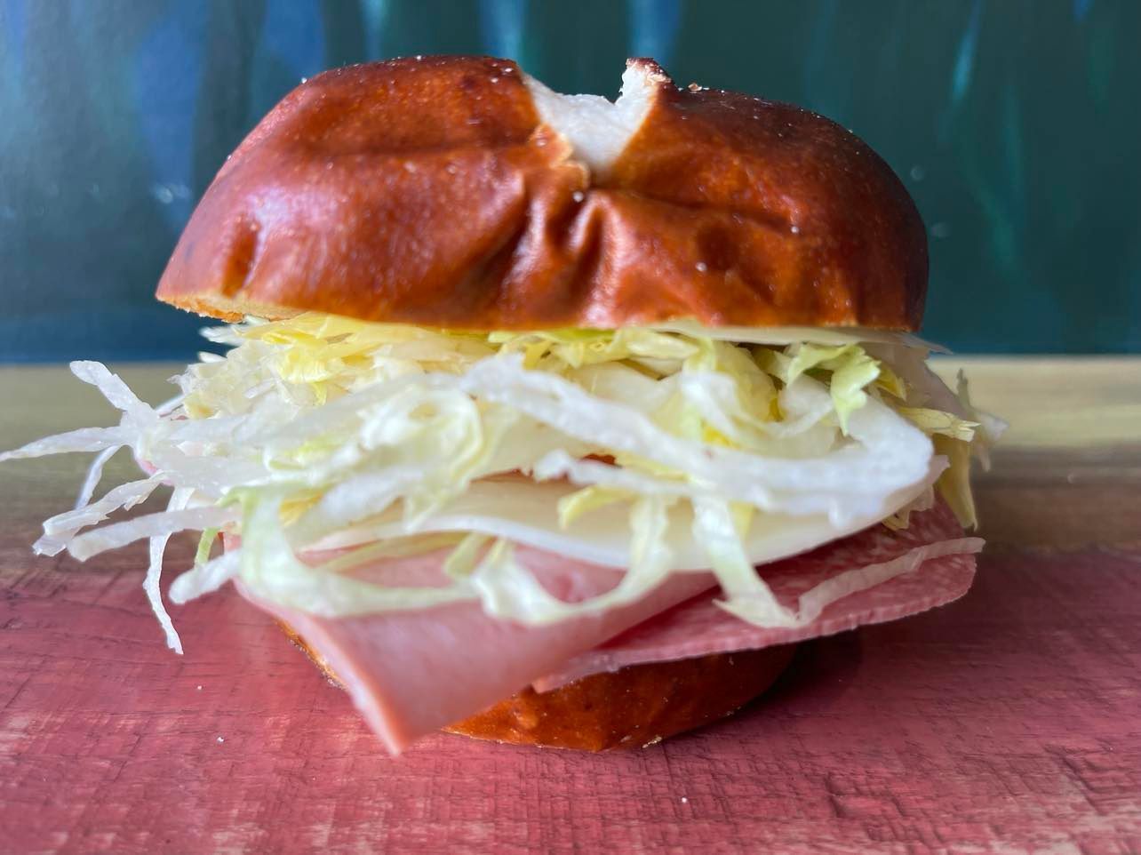 A ham and swiss cheese sandwich with shredded lettuce on a toasted pretzel bun, resting on a wooden surface.