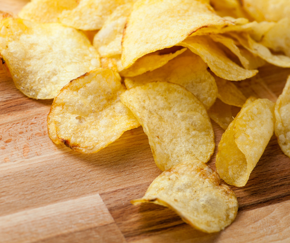 A pile of crispy, golden-brown potato chips scattered across a light wooden surface.