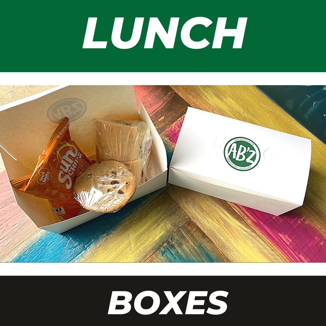 Two AB'z branded white lunch boxes on a multicolored surface; one is open, showing a snack bag and a cookie inside.