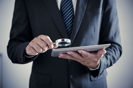 A man in a suit is holding a tablet and looking through a magnifying glass. A man in a suit is holding a tablet and looking through a magnifying glass.