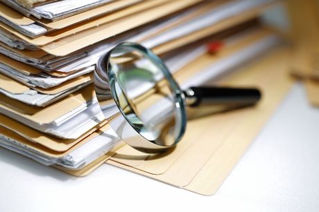 A magnifying glass is sitting on top of a pile of folders A magnifying glass is sitting on top of a pile of folders