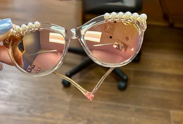 A person is holding a pair of sunglasses with pearls on them.