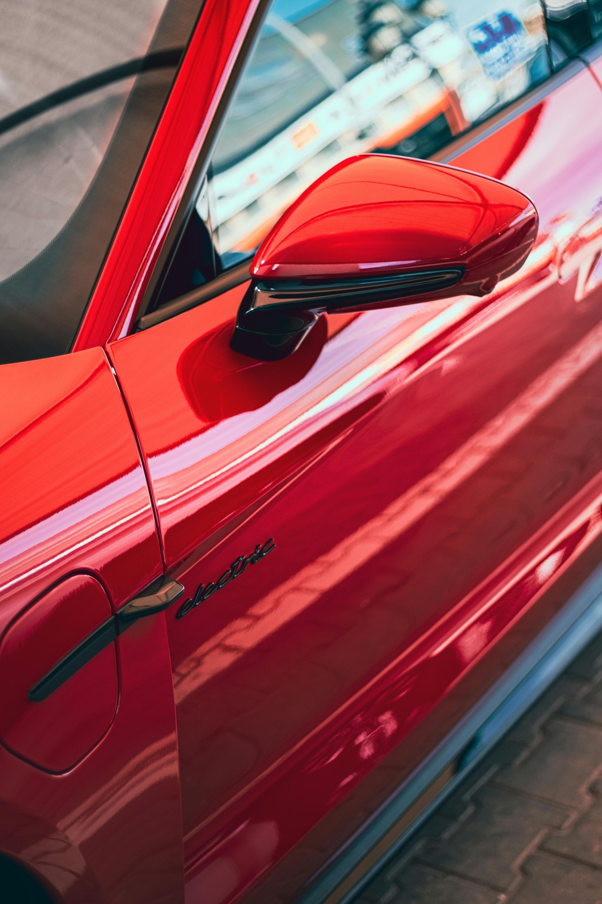 Close-up of a red car door and side mirror parked on a street