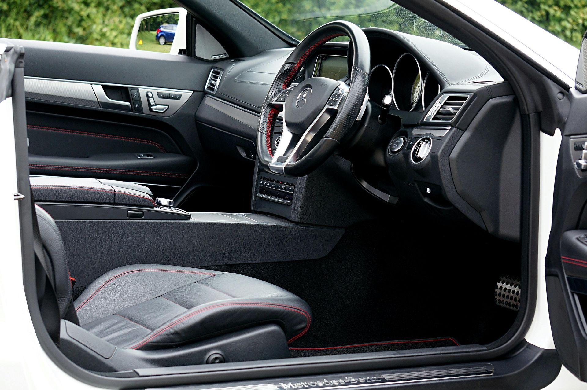 Interior of a black sports car with red-trimmed seats and steering wheel, door open to the side