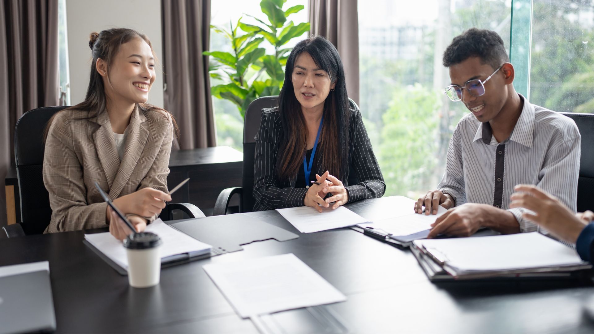 Three coworkers discussing papers at a conference table in a bright office