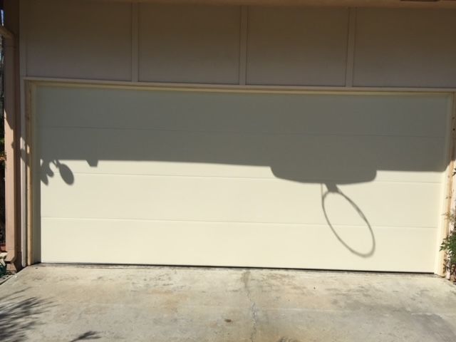 Beige garage door with basketball hoop shadow on a concrete driveway.