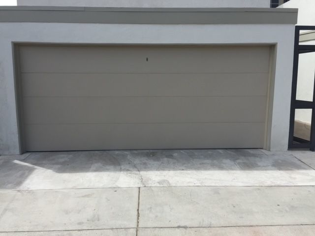 Tan garage door, mounted on a building with a concrete driveway in front.