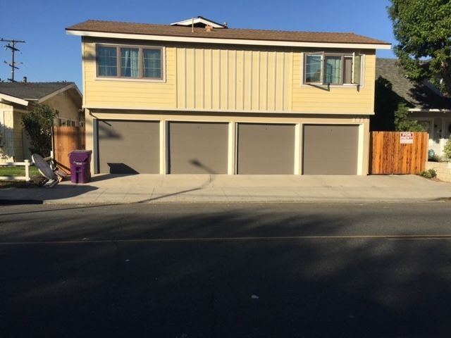 Yellow house with three garage doors. Brown trim, tan siding, open window, and a driveway.