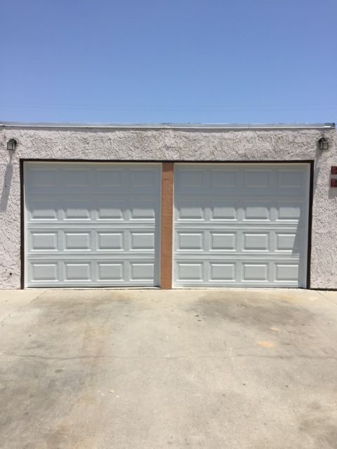 Two white panel garage doors side-by-side on a stucco building under a clear blue sky.