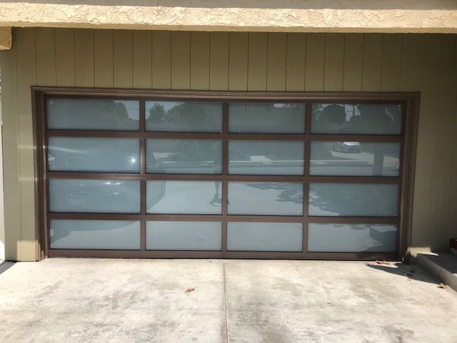 Brown-framed garage door with frosted glass panels, closed. Beige siding and concrete driveway.