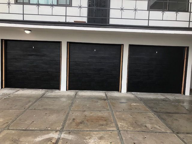 Three black garage doors with white trim on a concrete surface. Building exterior.