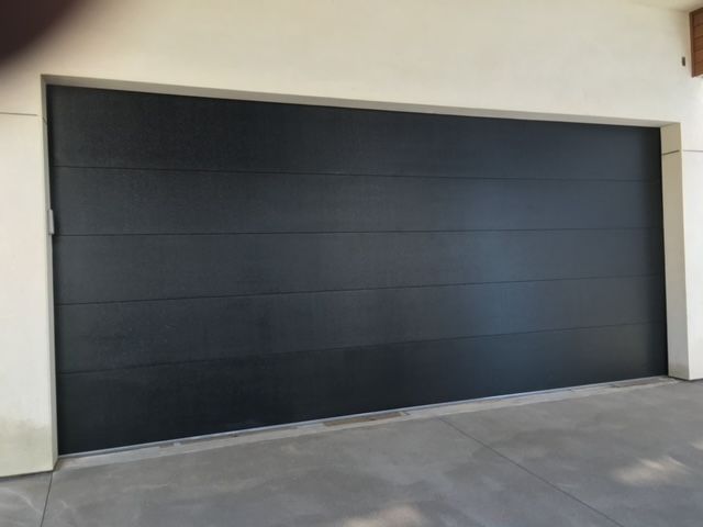 Black garage door with horizontal lines. Light-colored concrete driveway and frame.