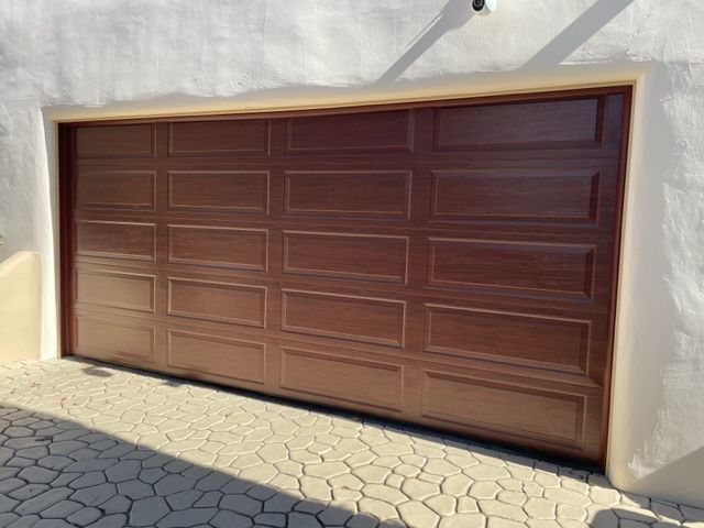 Brown garage door, closed, with a grid pattern, set in a white wall with a stone driveway.