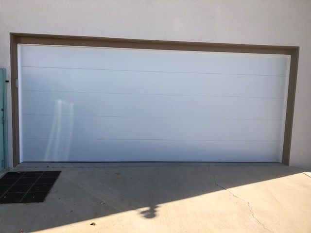White garage door with brown frame, set in a white wall, and concrete ground.