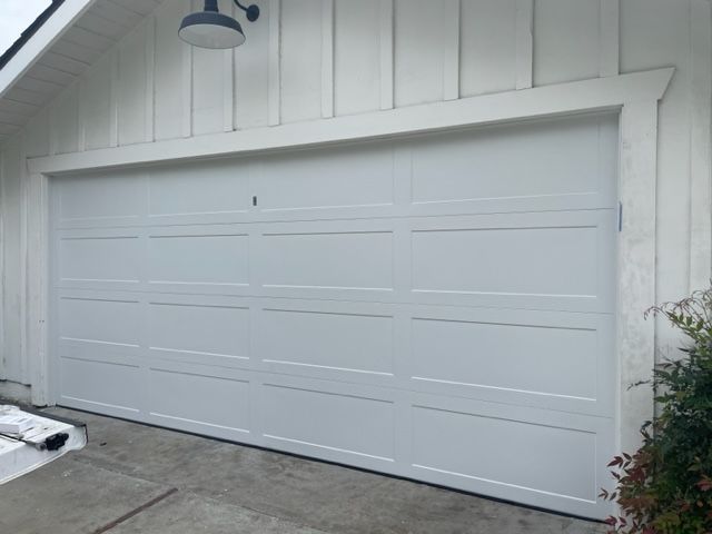White garage door on a white house, with a light fixture above.