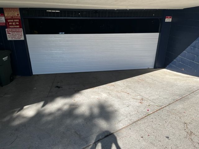 White garage door, partially closed, with shadows on the concrete driveway.