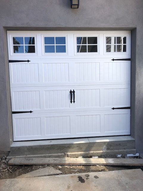 White garage door with window panels and black hardware, set in a gray wall.