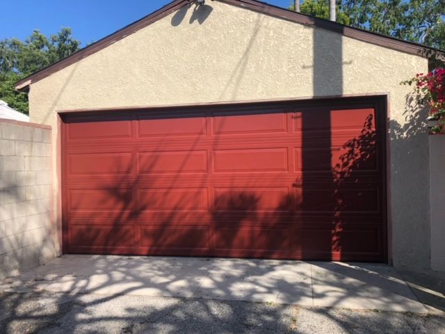 Red garage door on a stucco building; shadows from trees on the driveway.