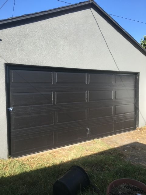 Dark brown garage door on a light gray building, with green grass in front.