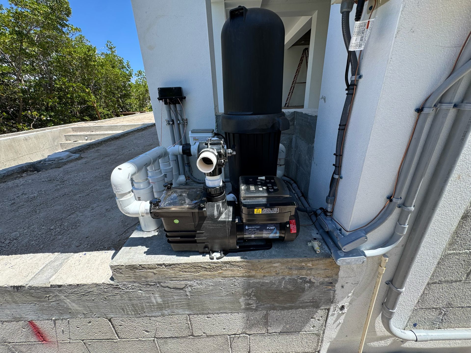 Black water pump system on a concrete foundation, with white pipes and a tall black tank, outdoors.
