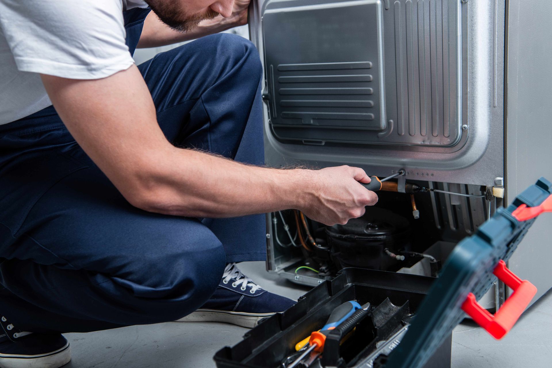Technician kneeling beside an appliance, using a wrench to repair its lower panel.