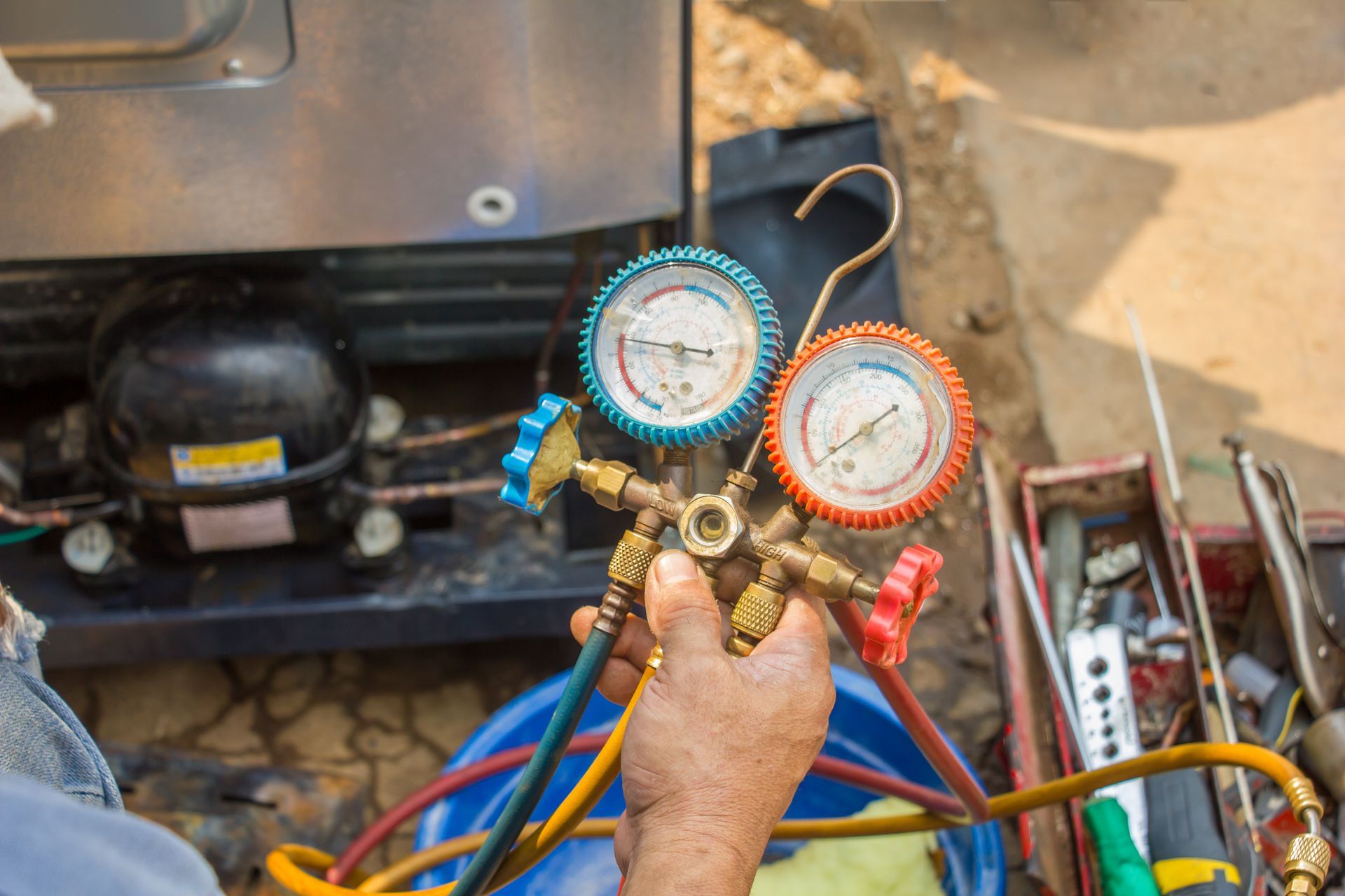 Technician holding HVAC manifold gauges with blue and red hoses near outdoor unit