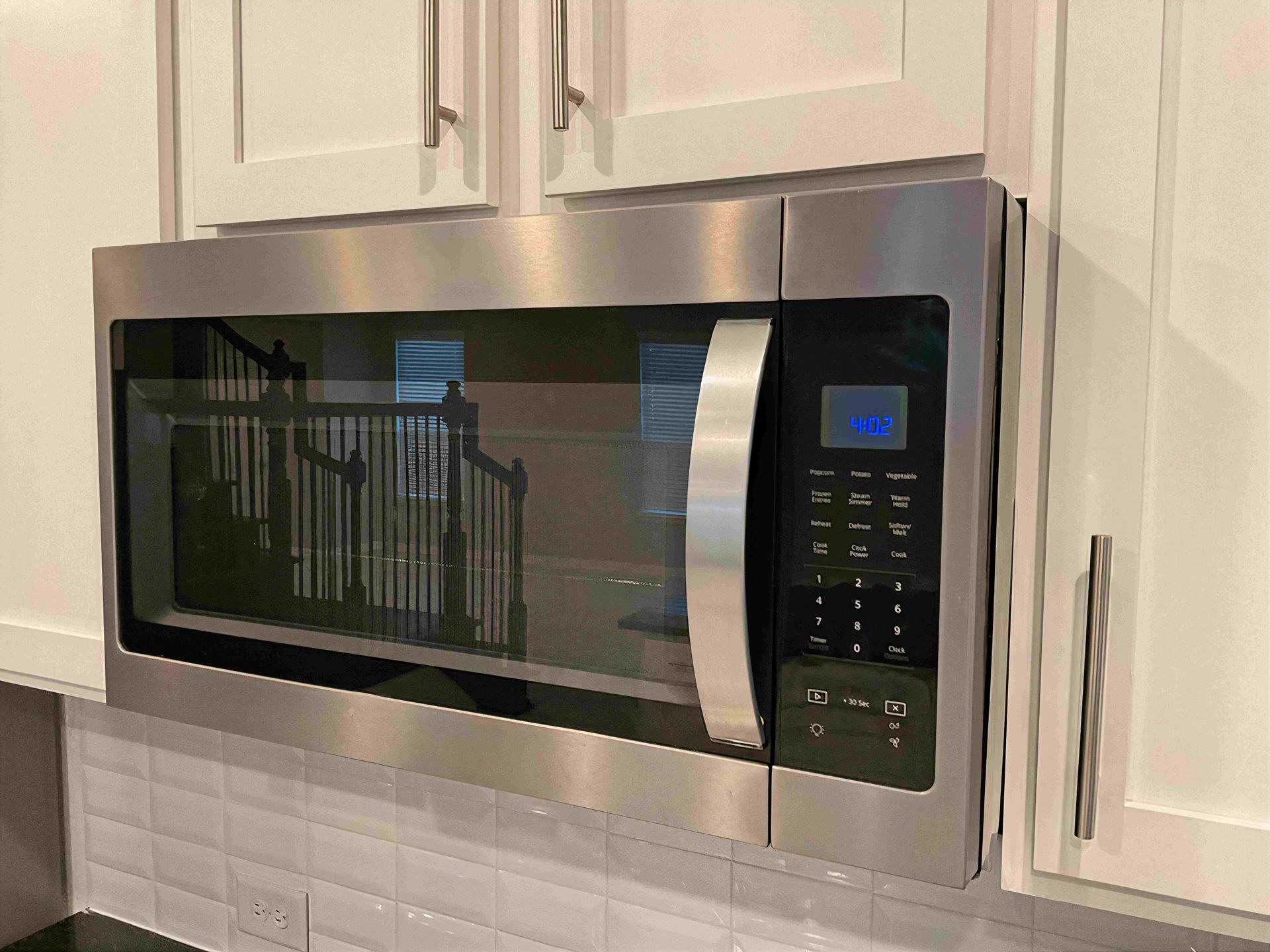 Stainless steel microwave built into white kitchen cabinets above a tiled backsplash