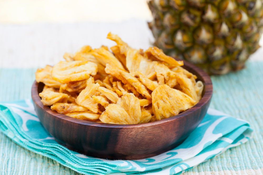 A Wooden Bowl Filled With Dried Pineapple Chips Next to a Pineapple — Mareeba Golden Dried Mangoes in Brisbane, QLD