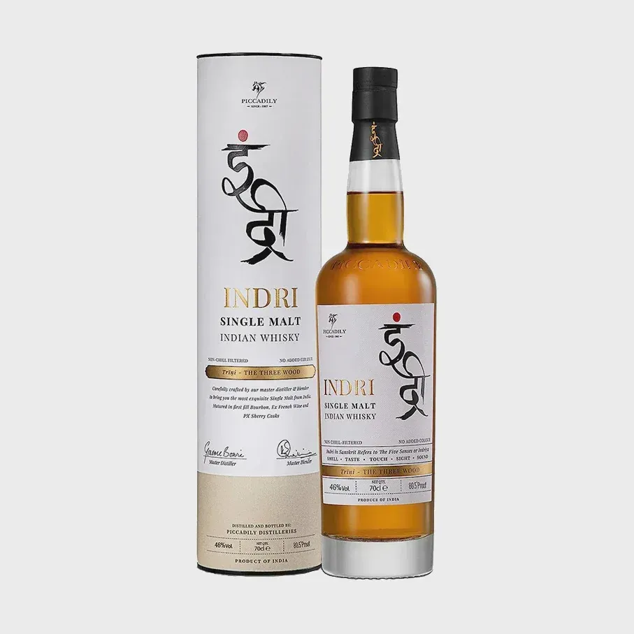 A bottle and a cylindrical box of Indri Trini Indian Single Malt whisky with white labels and gold accents.