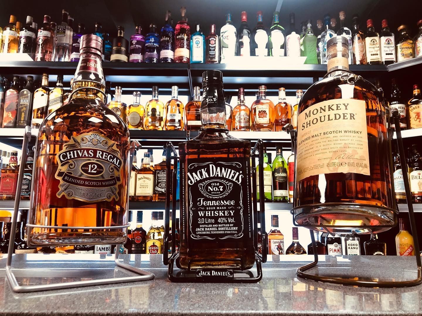 Three bottles of whiskey are sitting on a counter in a liquor store.