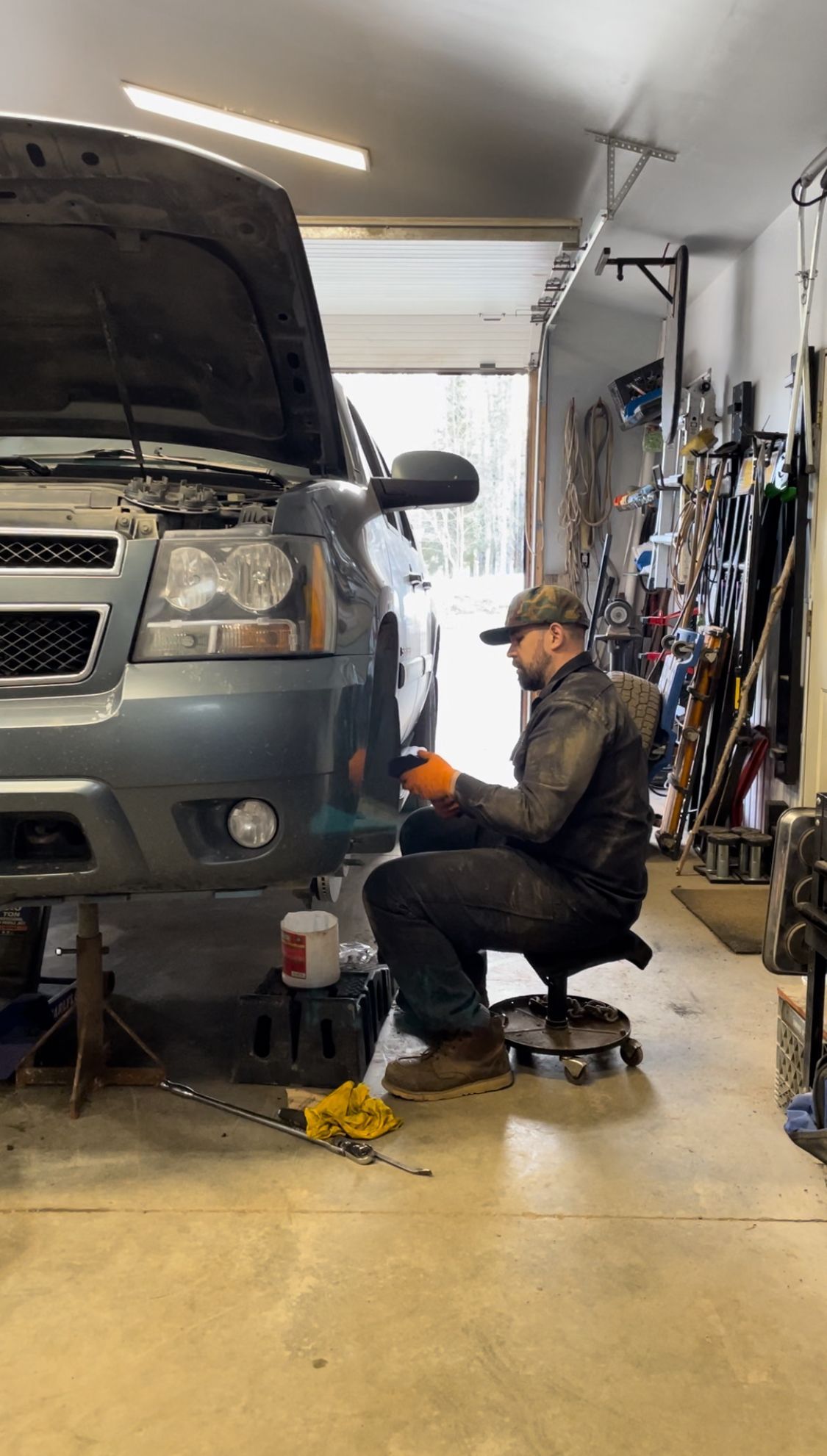 Auto Technician Inspecting Engine Bay Of Silver Truck Inside Workshop | Hatch Peak Motorworks
