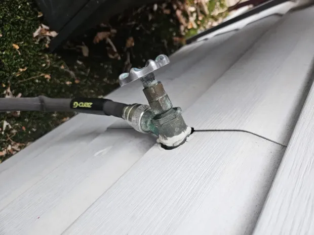 Garden hose connected to a cracked white vinyl surface near the edge of a deck or pool cover