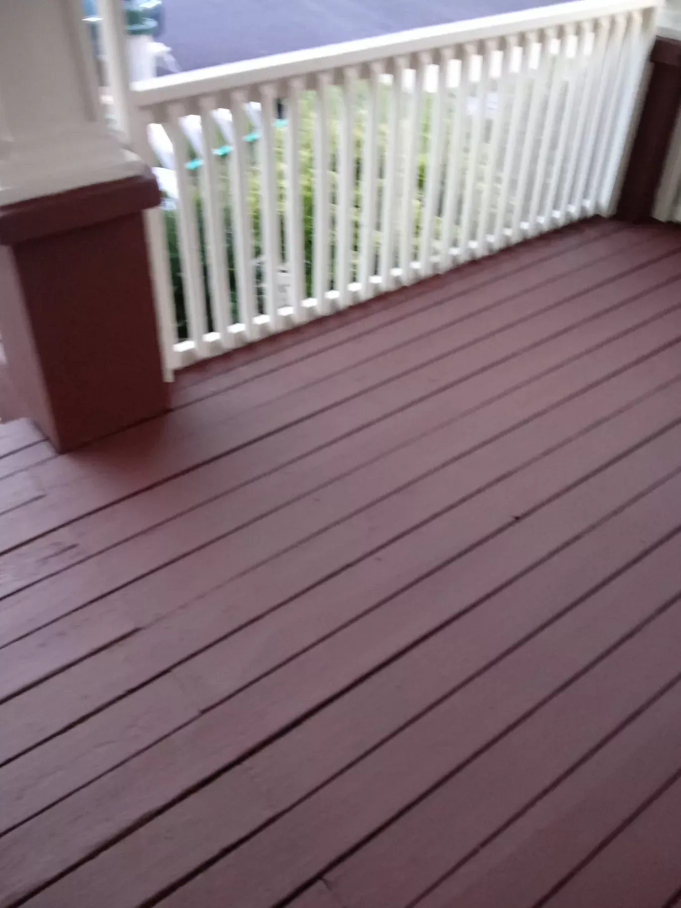 Brown wooden porch floor with white railing and a view of greenery beyond