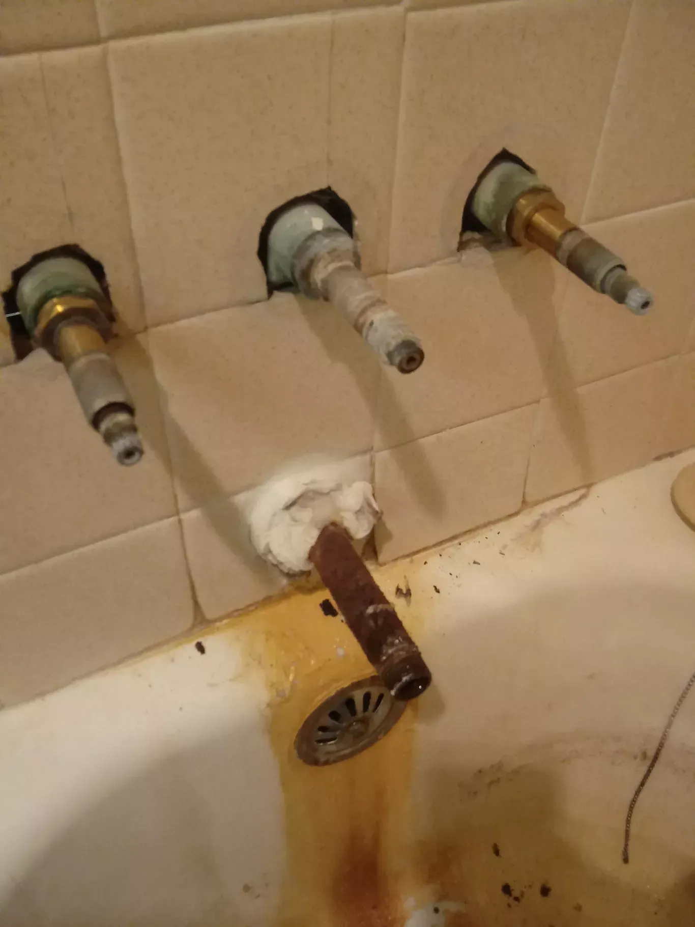 Old bathtub with exposed wall pipes and a rusted, broken faucet dripping stains onto the tub.