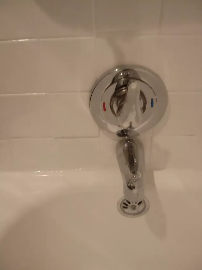 Chrome shower control handle on a white tiled wall with red and blue temperature markers