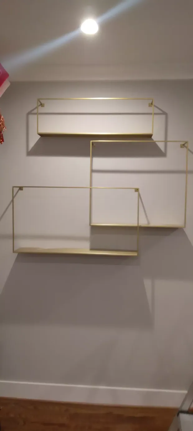 Wall-mounted geometric gold shelves on a white wall above a wooden floor.
