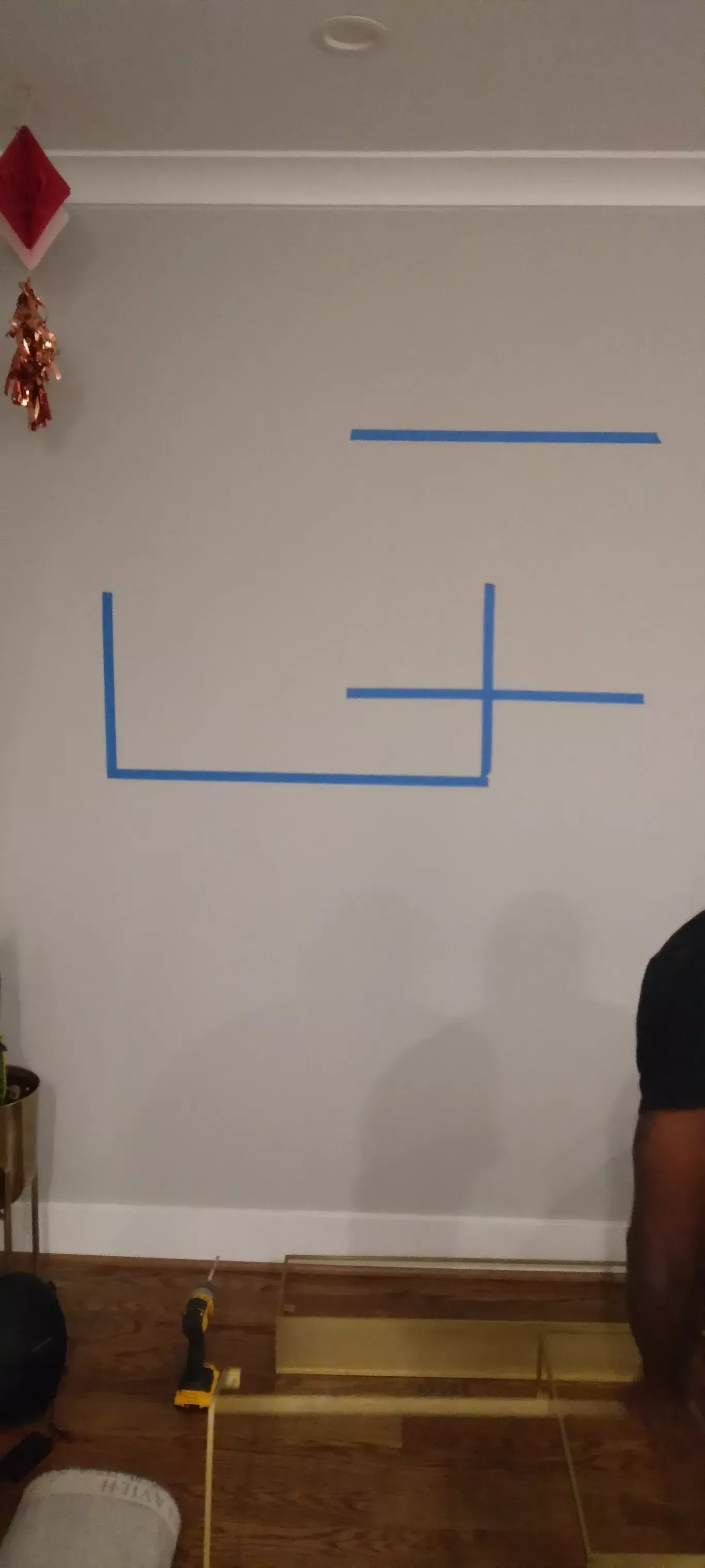 Blue tape markings on a white wall above a wooden bench, with a person partly visible at right.