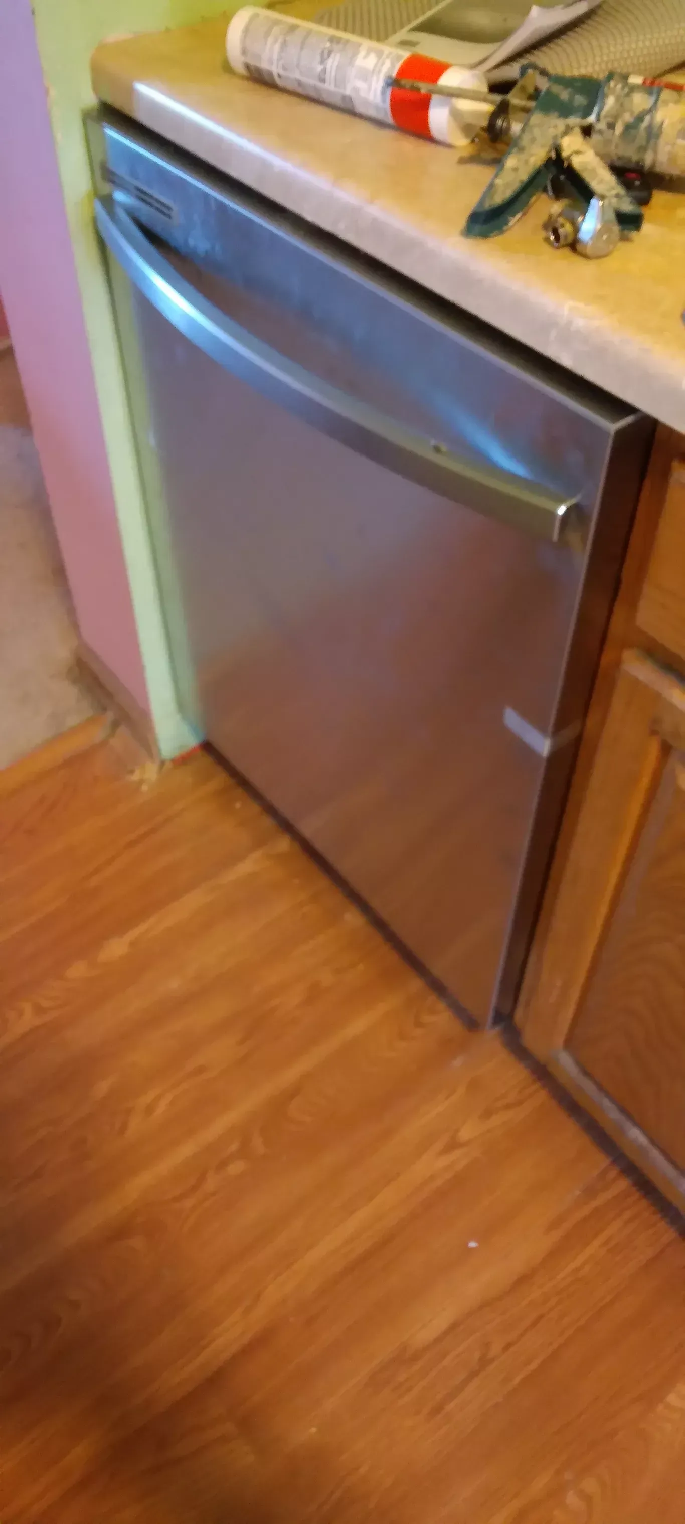 Small stainless steel dishwasher built into a kitchen cabinet beside a wooden floor and countertop.