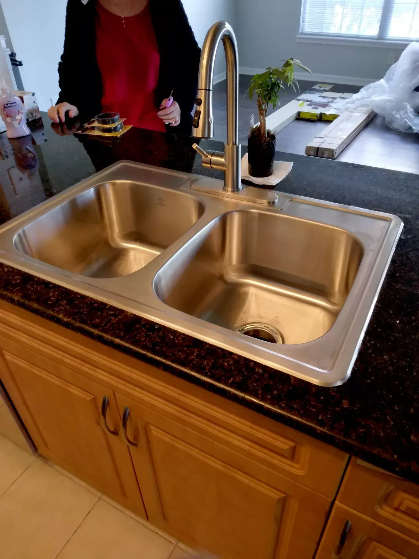 Kitchen sink with double basins, tall chrome faucet, and a person standing nearby.