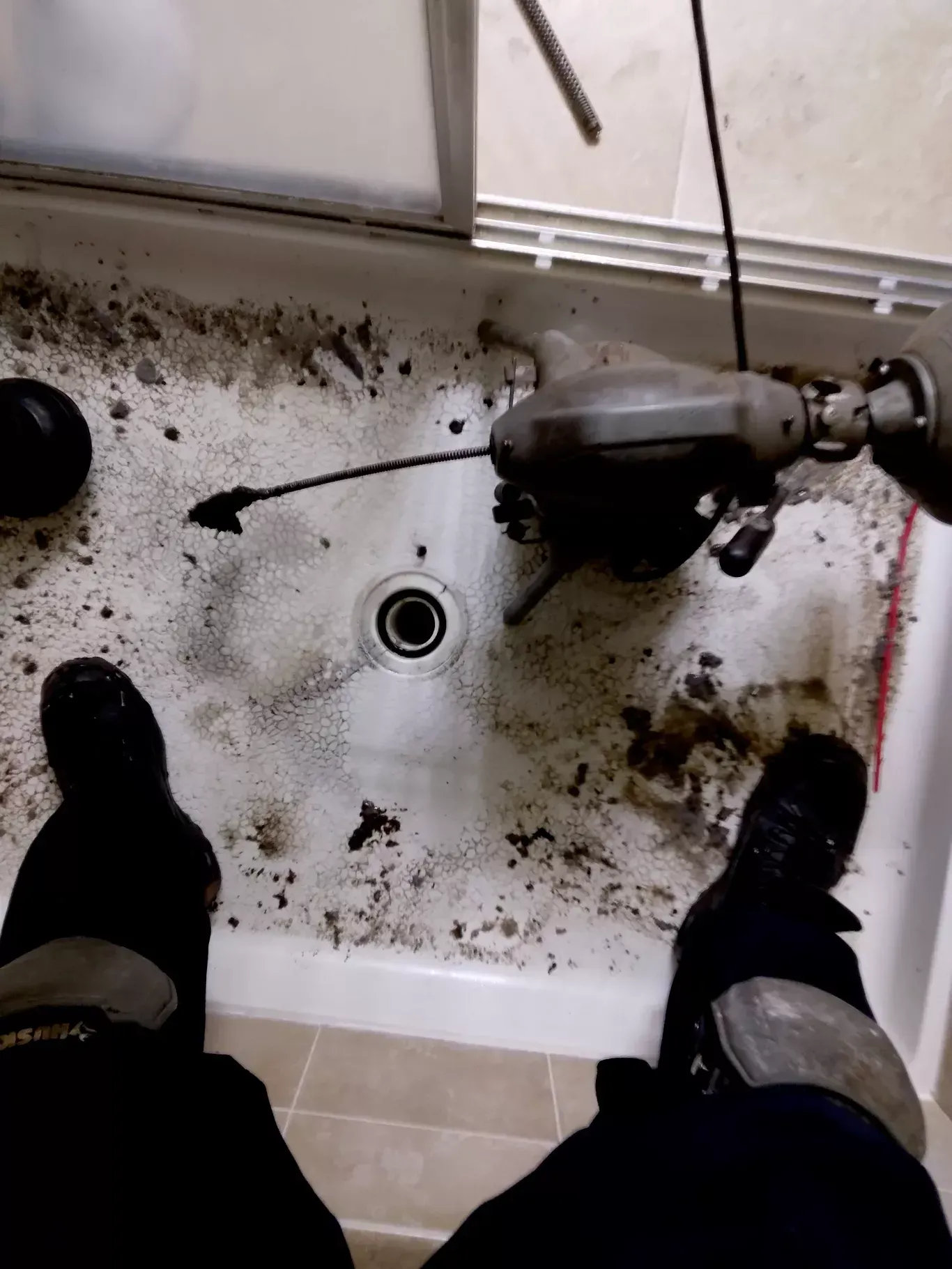 Dirty sink basin with drain and exposed pipe, seen from above with feet on either side.