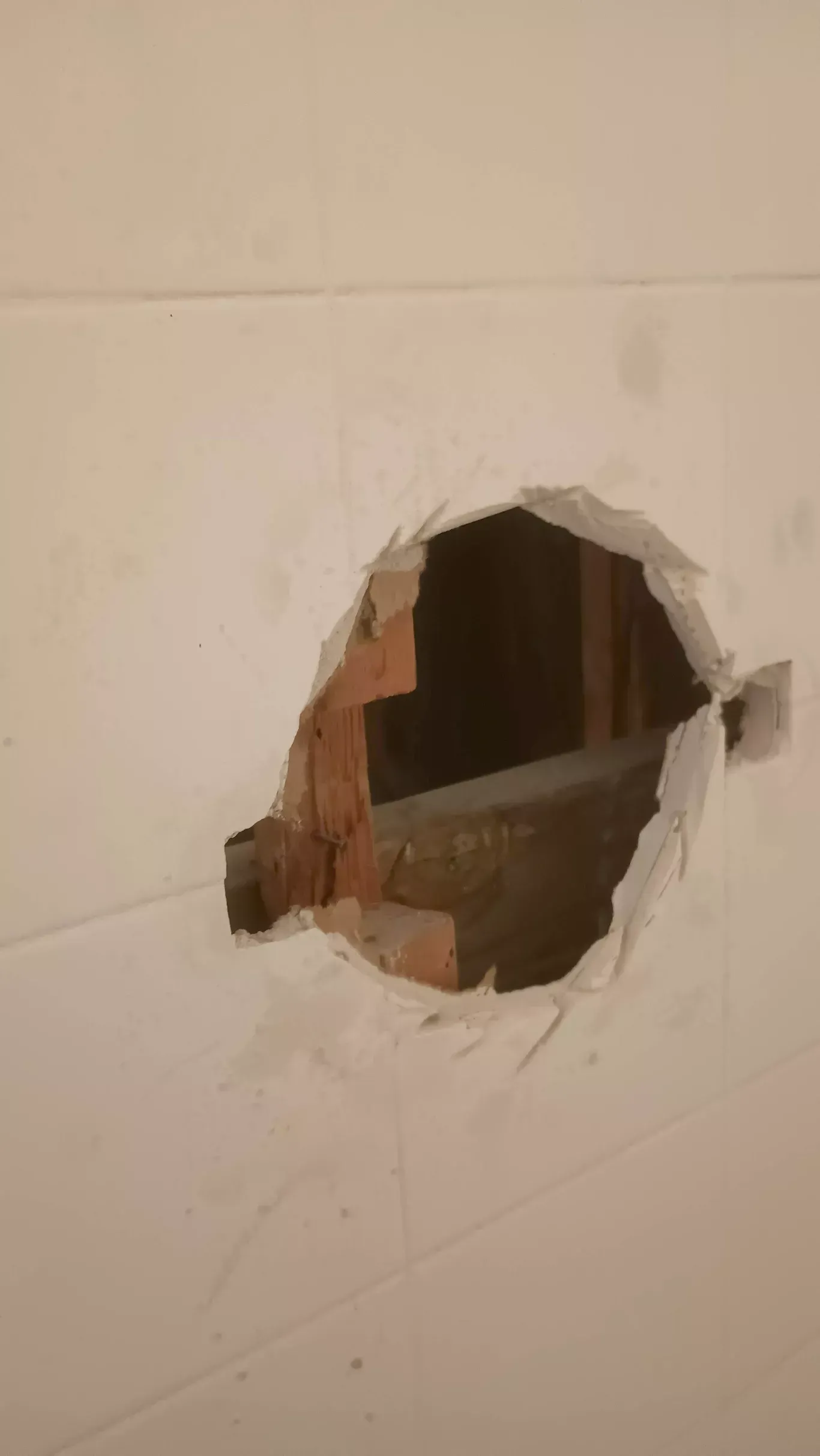 Broken white wall with a large circular hole exposing the wooden studs behind it