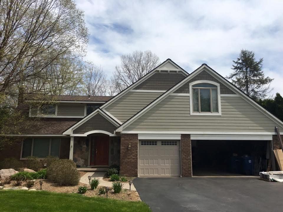 House exterior with a tan garage door, green siding, and a red front door.