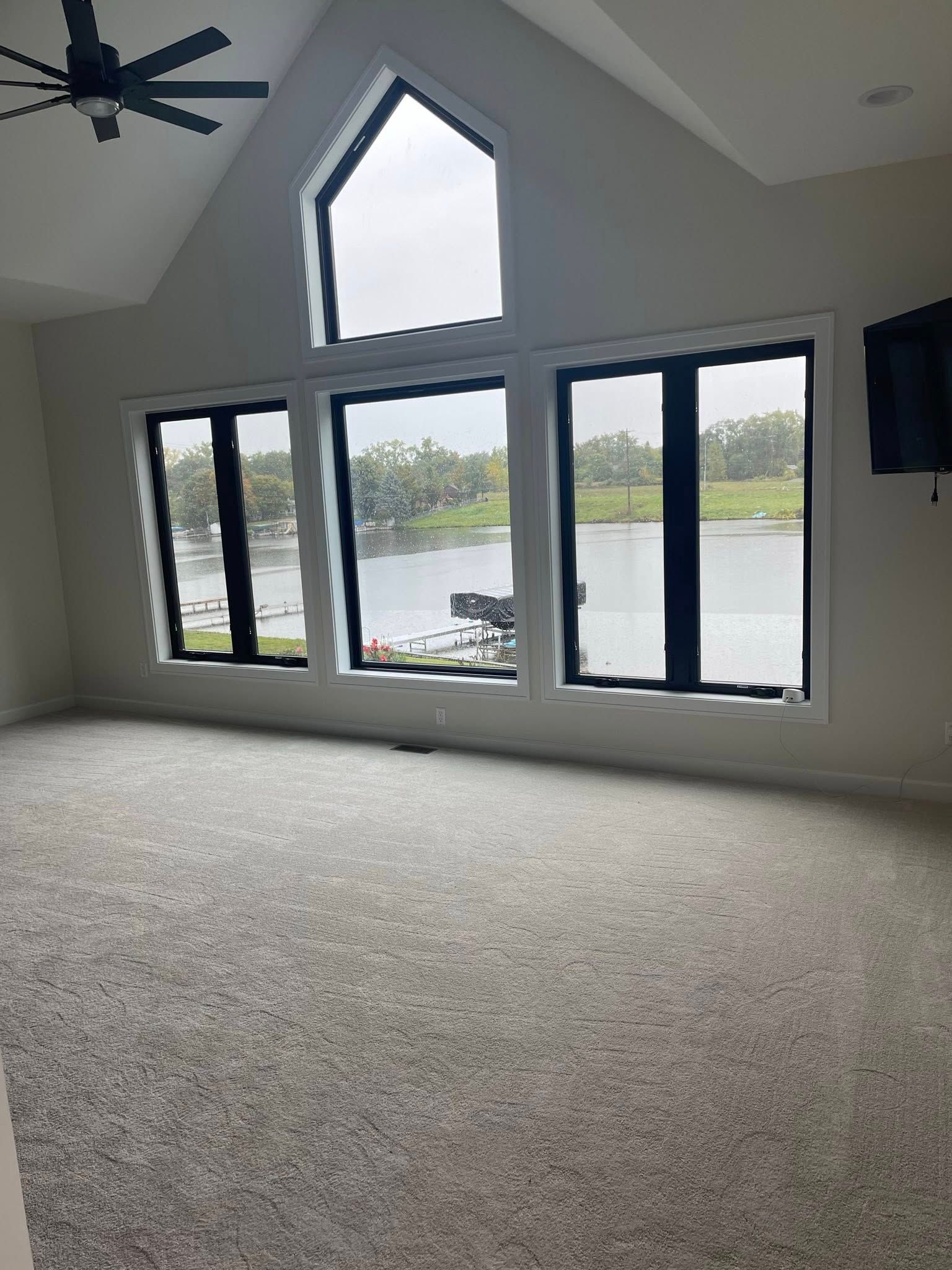 A large, empty room with gray carpet and large windows overlooking a body of water.